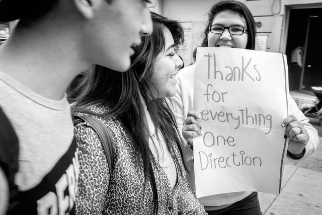 A woman on the street in Mexico City, holding up a sign that reads "thanks for everything One Direction".