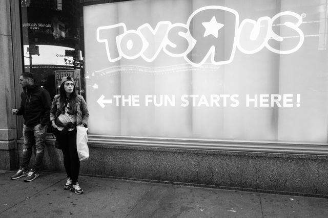 Two people standing next to a Toys R Us sign that says "the fun starts here".