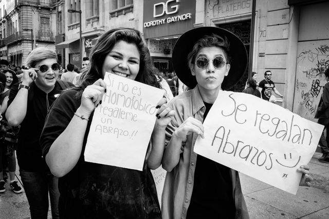 Two people holding signs on the street in Mexico City, which read "si no es homofóbico regáleme un abrazo" (if you're not homophobic, give me a hug) and "se regalan abrazos" (free hugs).