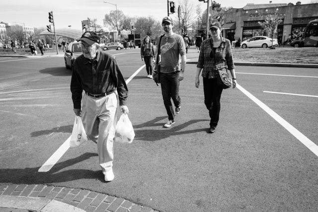 A smiling older man carrying grocery bags crossing Pennsylvania Avenue SE near Eastern Market.