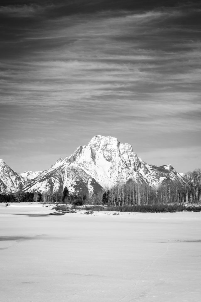 Mount Moran, seen in early spring under whispy clouds, in front of a still-frozen Oxbow Bend.