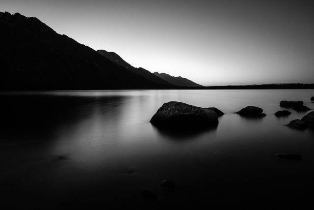 Jenny Lake after sunset. In the foreground, a few big boulders in the water; in the foreground, the Teton Range.