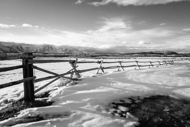 A wooden fence in the snow, with the Teton range seen in the background.