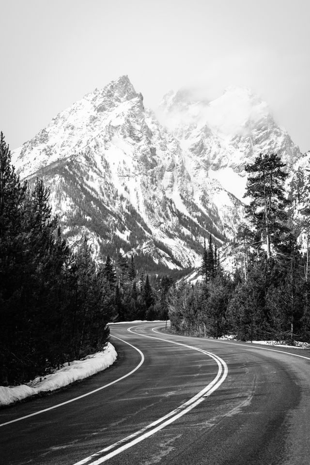 The Cathedral Group of the Teton Range, on a cloudy, foggy spring day, seen through a winding road.