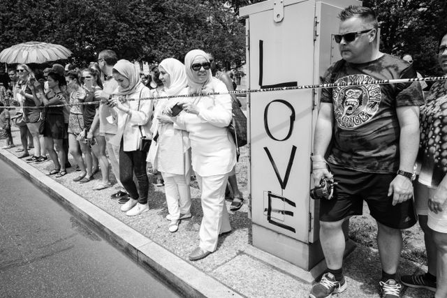 Americans watching the Independence Day parade in Washington, DC. Next to them, a utility box is graffiti'd with LOVE in big letters.