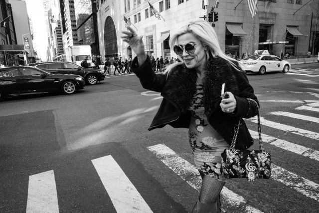 A woman waving and smiling as she crosses the street on New York's Fifth Avenue.