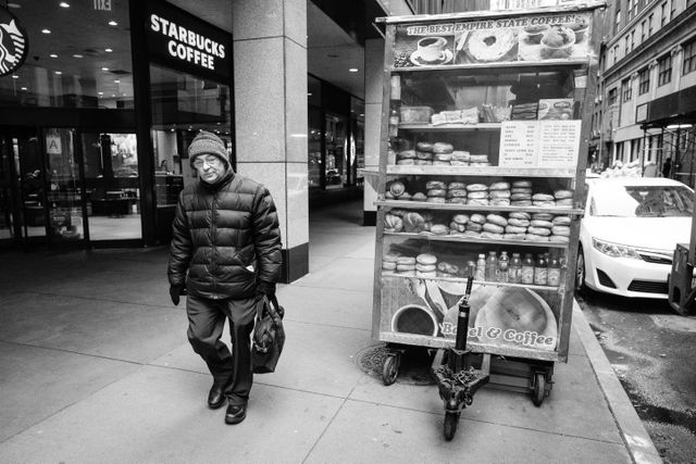 A man walking past a bagel & coffee cart in the Financial District.