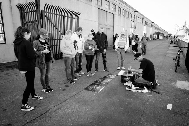 A group of tourists watching a street artist work with spray paint behind the Musée Mécanique in San Francisco.