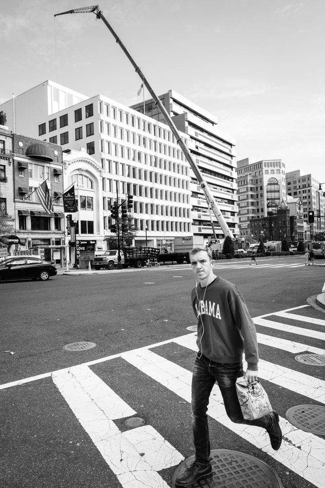 A man crossing the street in front of an enormous crane on Connecticut Avenue NW.