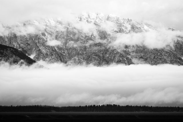 The Teton range behind a low layer of clouds, covered in light snow after a storm.