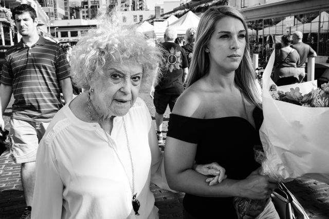 An older woman walking arm in arm with a younger woman holding a bouquet of flowers at Pike Place Market in Seattle.