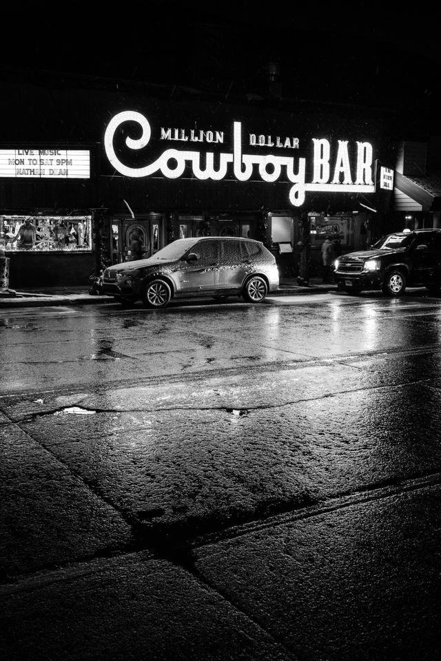 The sign of the Million Dollar Cowboy Bar lit up at night in Jackson, with its lights reflected off the wet pavement.