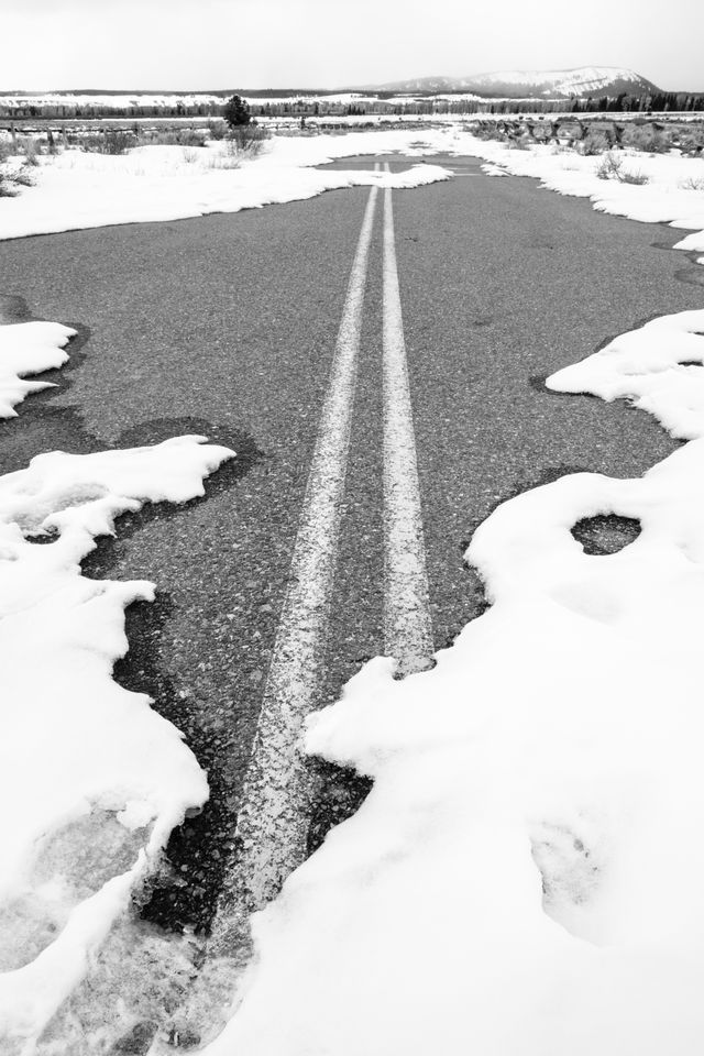 The pavement of a road partially covered in snow, leading to the Cunningham Cabin.