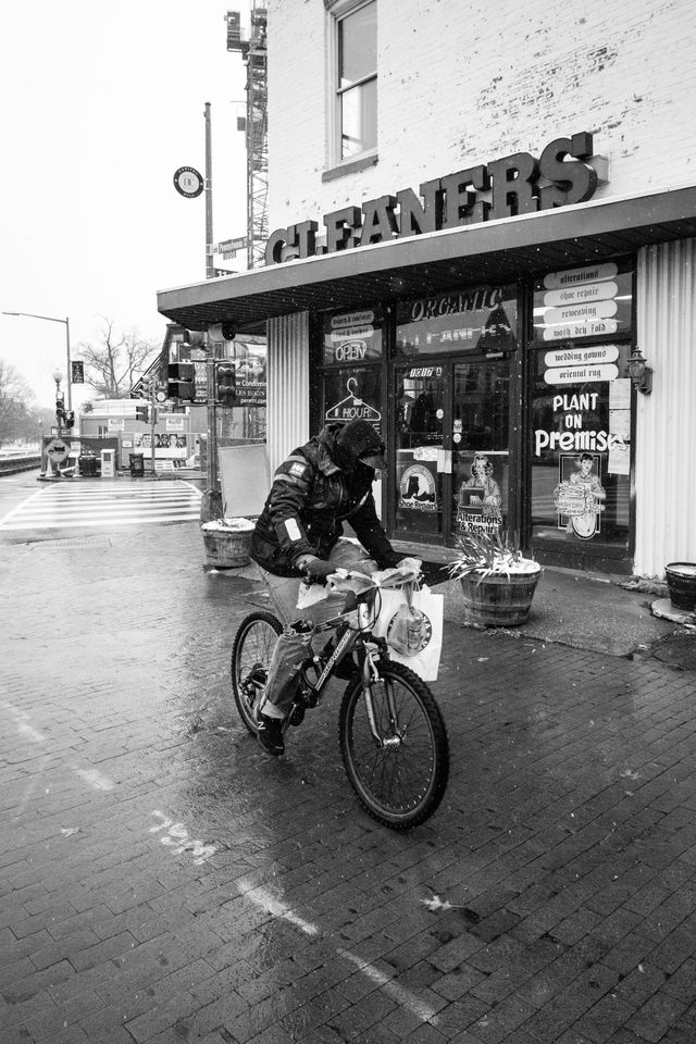 A man carrying a bag of Popeyes bikes past a dry cleaning business on Capitol Hill. 