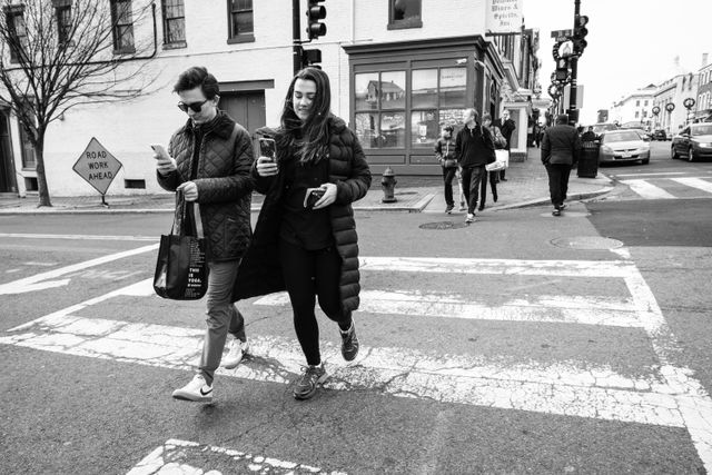 Two people crossing 31st street in Georgetown while looking at their phones.