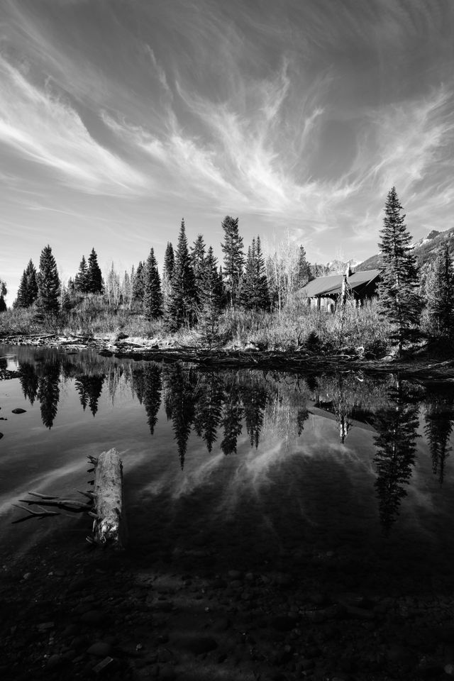 Trees, clouds and a private residence reflected off the waters of Jenny Lake at Grand Teton National Park.