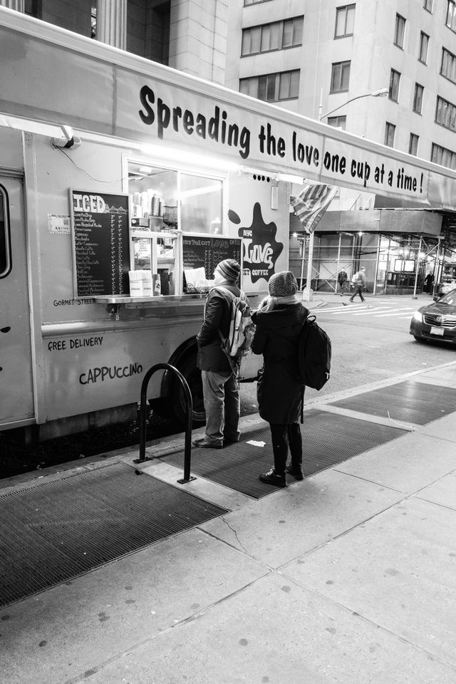 People buying coffee in front of a coffee truck with a sign that reads "spreading the love one cup at a time".