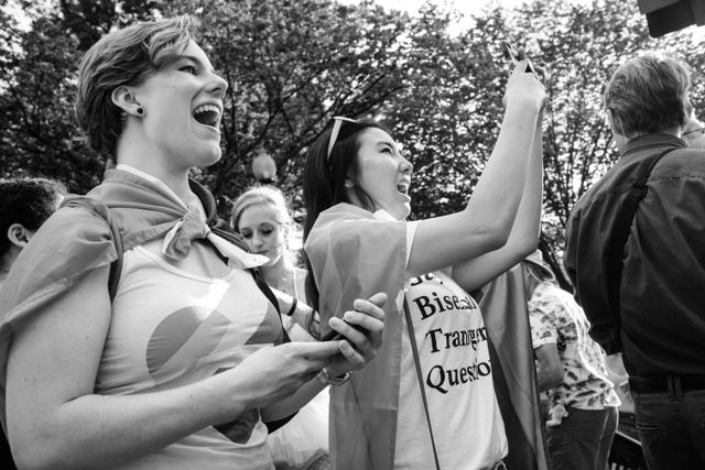 People in the crowd of the Capital Pride Parade, smiling and taking photos as the parade goes by.