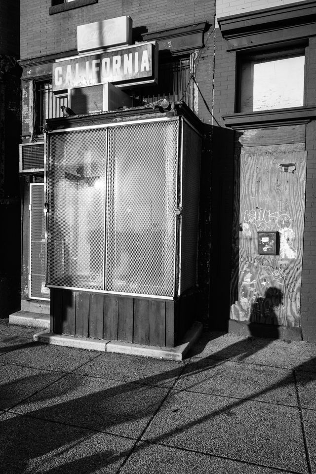 Shadows of people walking in front of a shuttered storefront with a California sign in Adams Morgan.