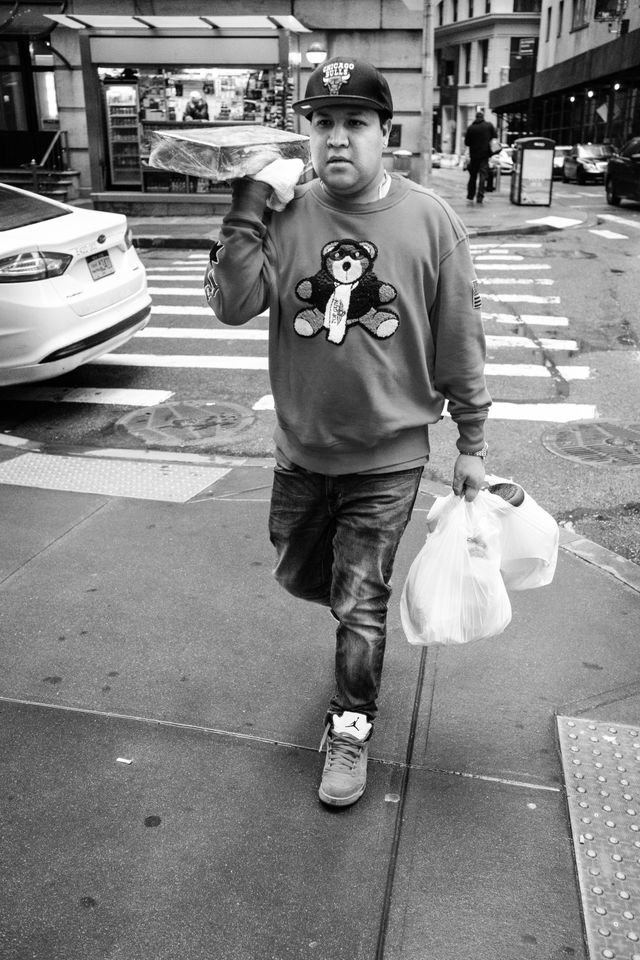 A man in a bear sweater and Chicago Bulls hat carrying food on William Street in New York.