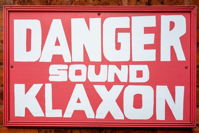 A red hand-painted sign that reads "danger sound klaxon".