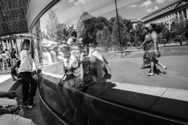 People reflected int he glass panel around the Oculus, at the National Museum of African American History and Culture.