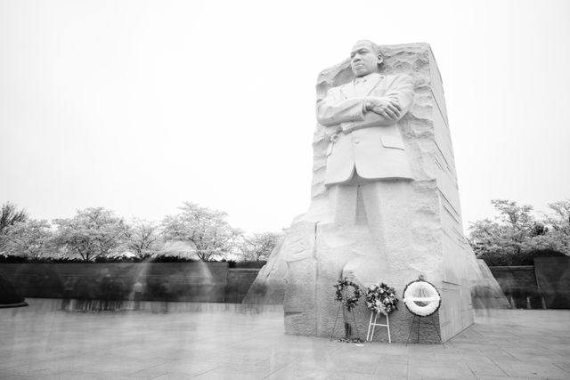 The Martin Luther King Jr. Memorial surrounded by blossoming cherry trees and crowds of people.