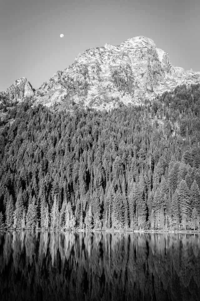 The Moon setting behind Symmetry Spire and Mount Saint John, with String Lake in the foreground.