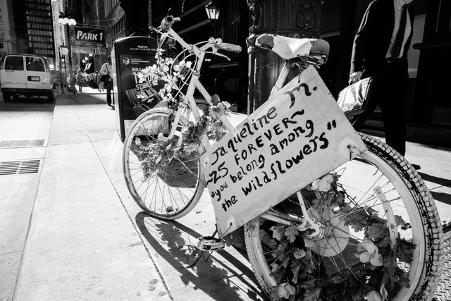 A bicycle covered in flowers with a sign that reads "Jaqueline M. ~25 forever~ 'you belong among the wildflowers'".