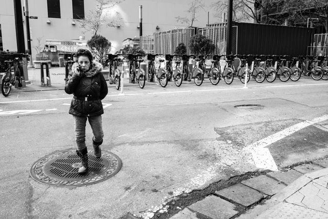 A woman crossing the street while talking on the phone, in front of a row of Citibikes.