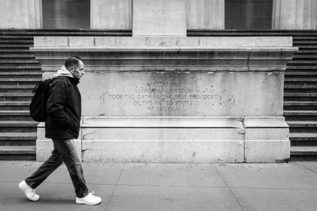 A man walking in front of the statue of George Washington at New York's Federal Hall.