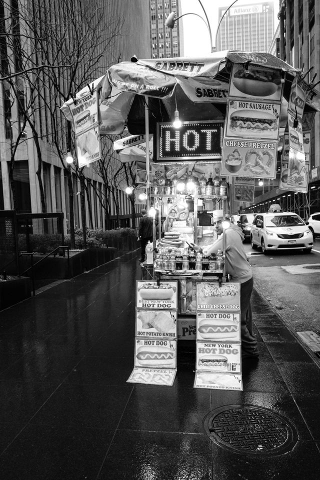 A person working a hot dog stand in the rain on Sixth Avenue in New York City.