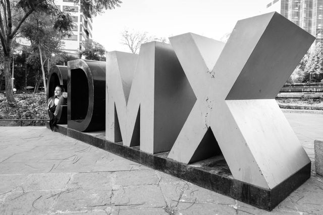 A woman sitting in a CDMX sign at Fuente de Cibeles.