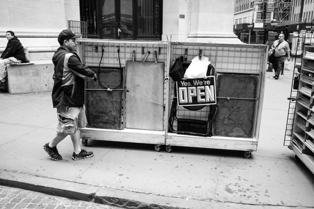 A street vendor pushing a merchandise cart with a sign that reads "yes, we're open" on Wall Street.