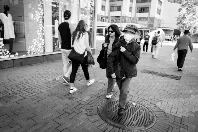 Women walking on Market Street, San Francisco; one of them is wearing a face mask.