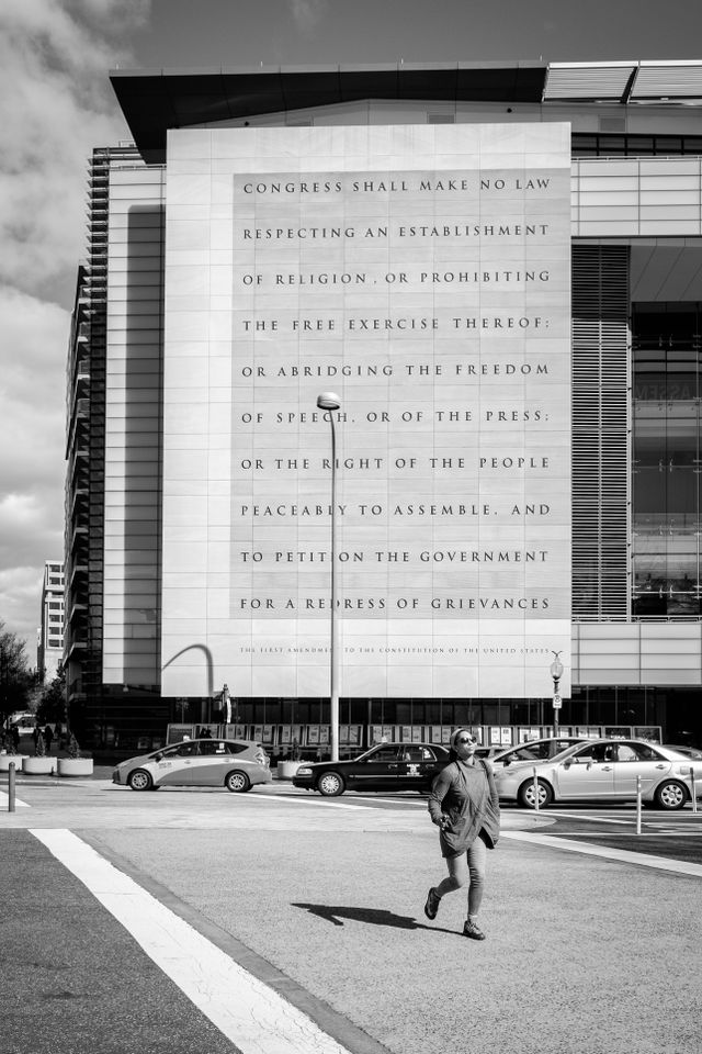 A pedestrian crossing Pennsylvania Avenue in front of the Newseum, which has the First Amendment engraved on its facade.