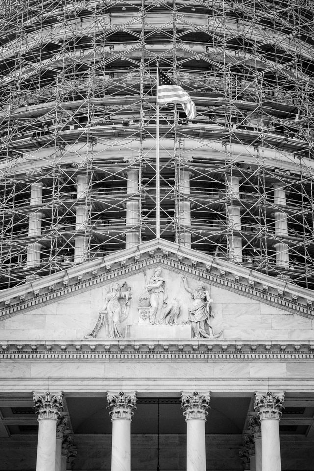 The pediment of the United States Capitol building on the West Front, with the dome covered in scaffolding.