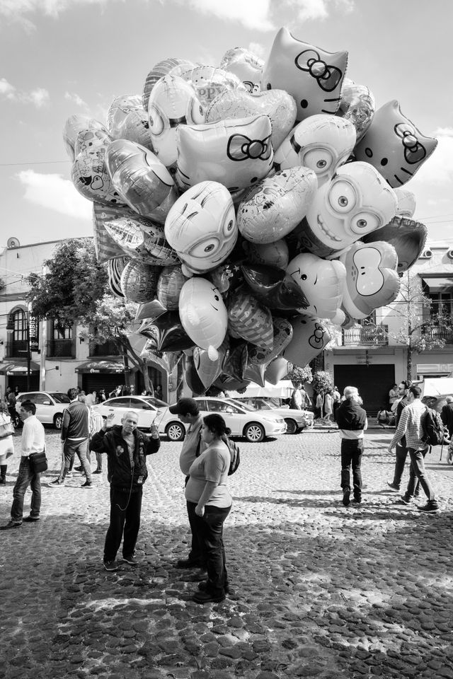 A salesman holding a bunch of balloons talking to customers.