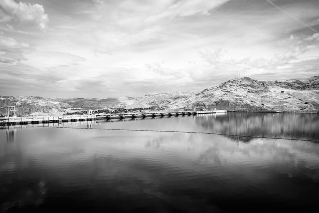 Roosevelt Lake and the Grand Coulee Dam. Hills and mountains are in the background. The sky is reflected in the surface of the water.