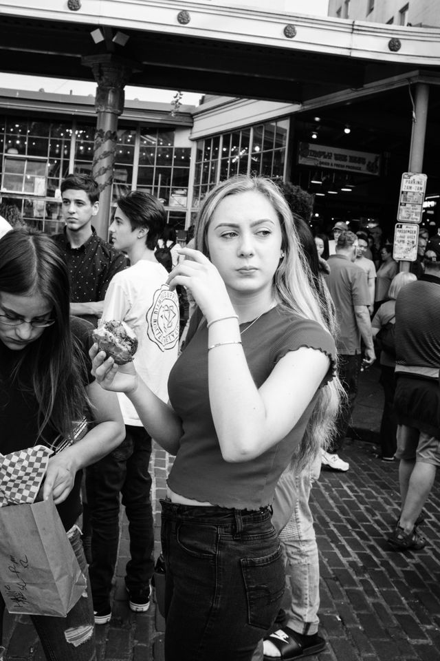 A young woman eating some kind of sandwich on the street near Pike Place Market.