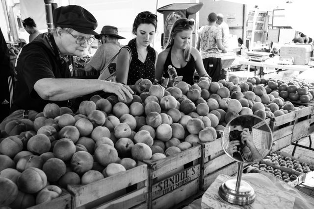 Three women shopping for peaches at Eastern Market in Washington, DC.