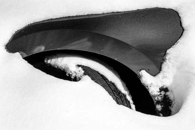 The wheel well of a car completely buried in snow.