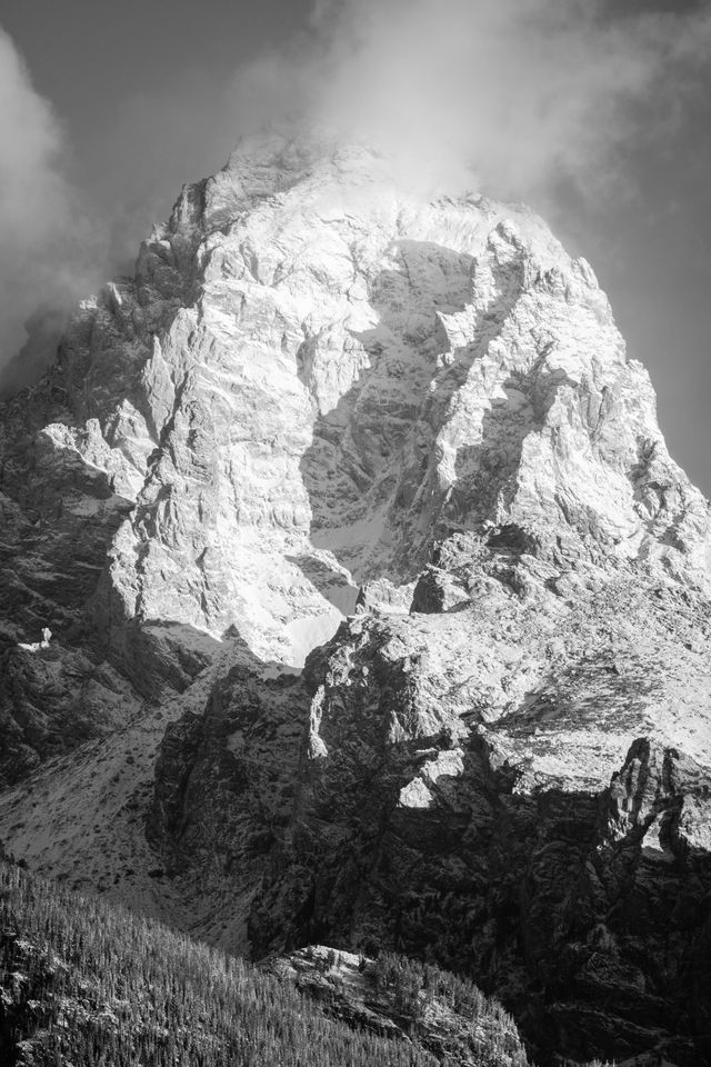 Grand Teton, covered in the first big snowfall of the fall, at sunrise, with clouds around its summit.