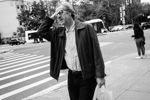 A man carrying a bag and grimacing while walking along East Houston Street in Manhattan.