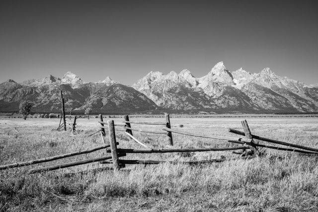 A rustic wooden fence in a grassy field with the Teton Range in the background.