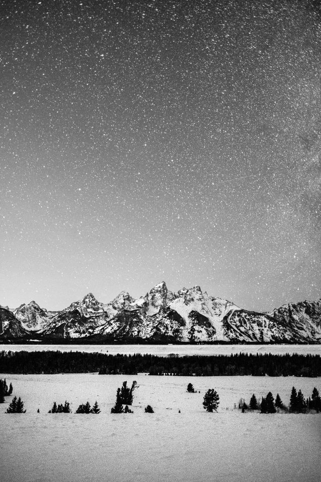 The snow-covered Teton Range seen at night under a starry sky, from the Teton Point Turnout.