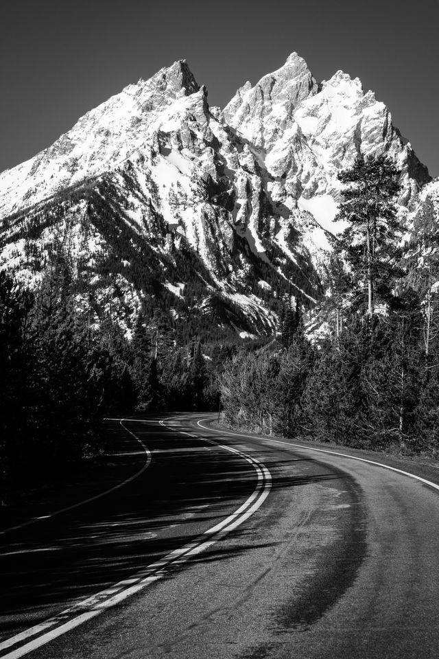 The Cathedral Group of the Teton Range, on a clear, sunny spring day, seen through a winding road.